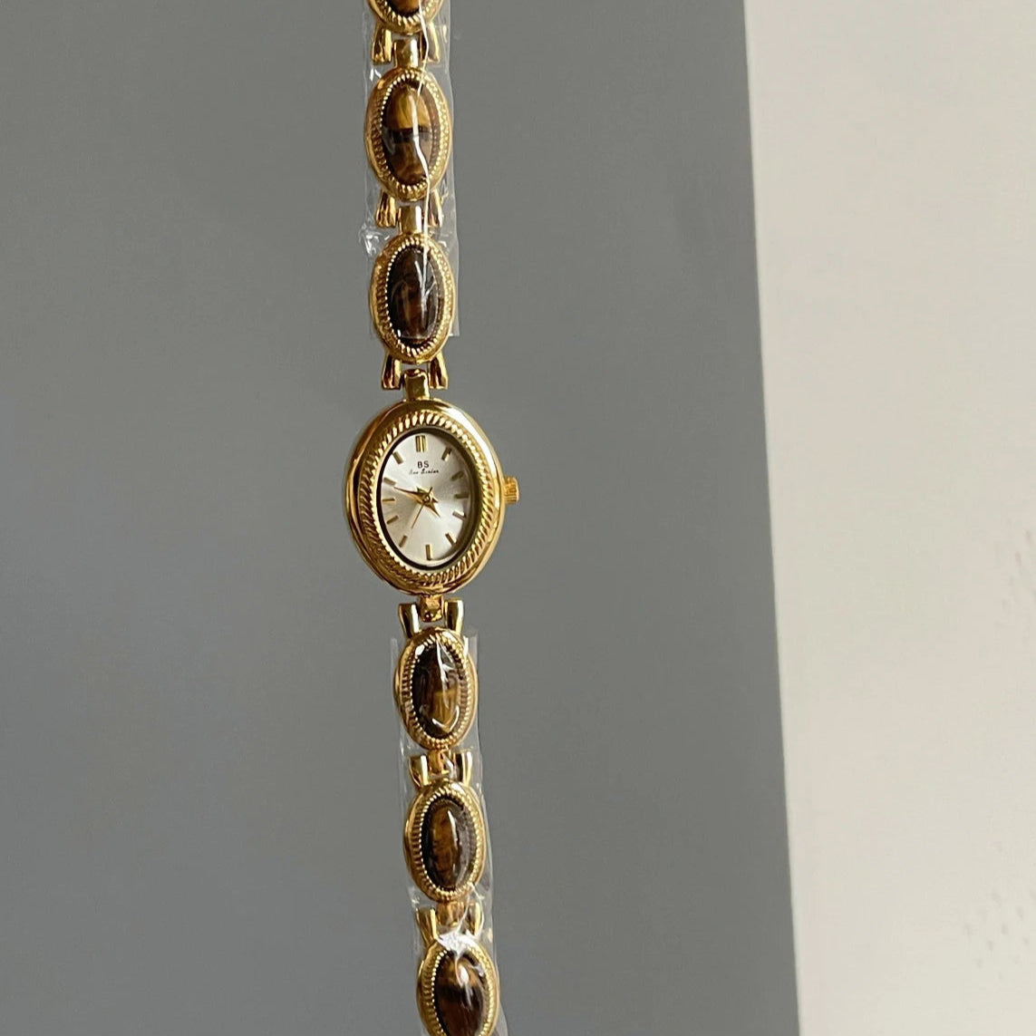Gold bracelet with a watch face on a gray background