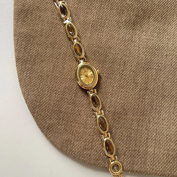 Gold bracelet with a watch face on a brown fabric background
