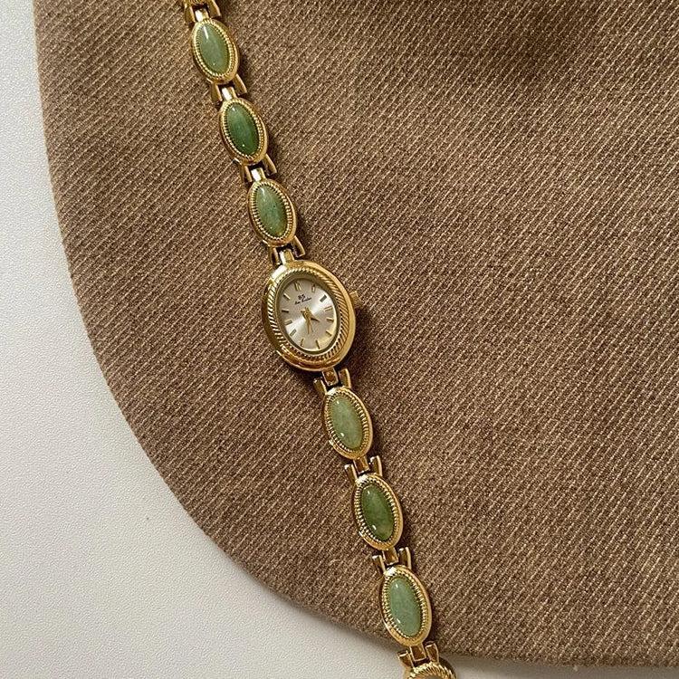 Gold bracelet with green stones on a brown fabric background