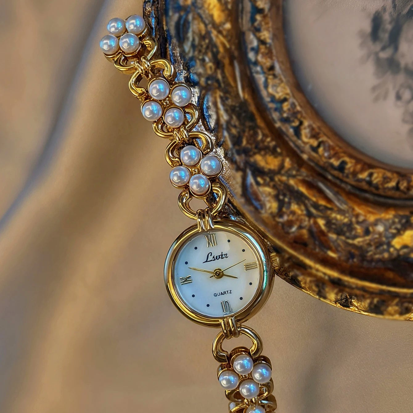 Vintage-style gold watch with pearl chain against an ornate gold frame background