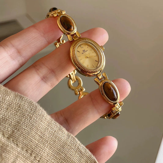 Gold watch with gemstone accents held in a hand against a neutral background