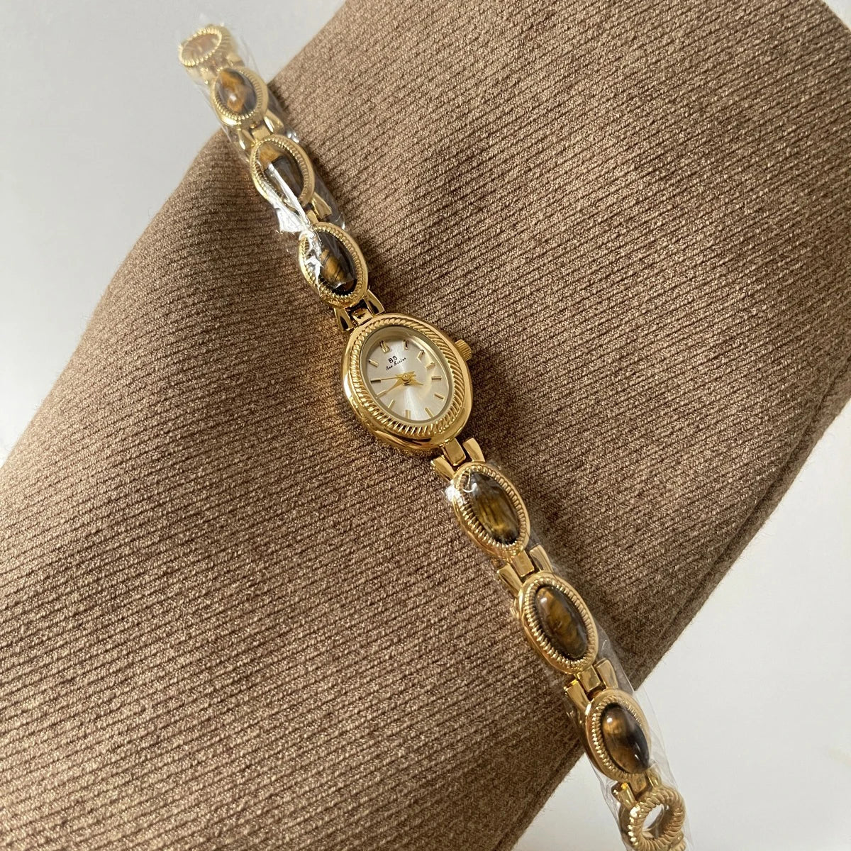 Gold bracelet with a watch face on a brown textured surface