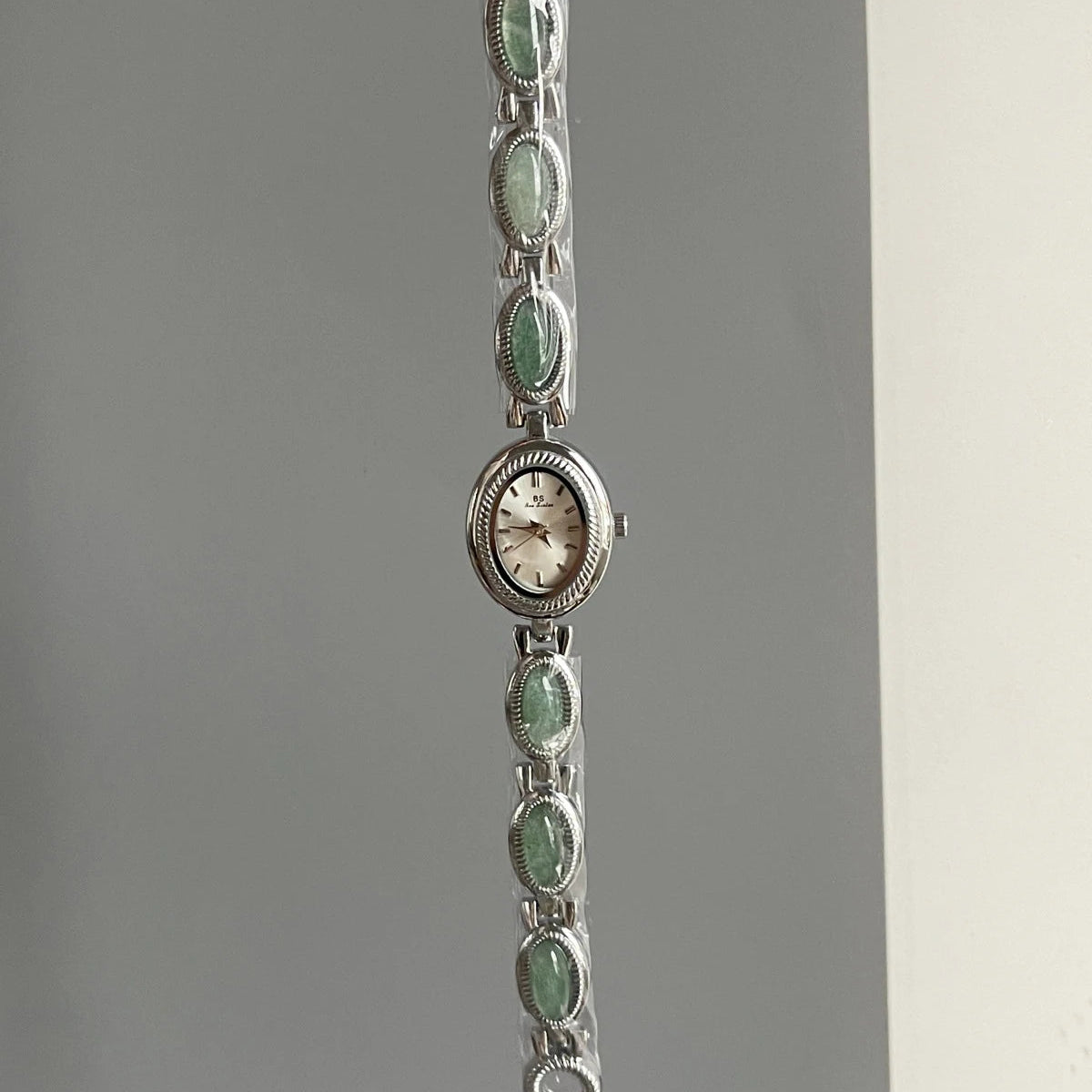 Silver bracelet with green gemstones on a gray background